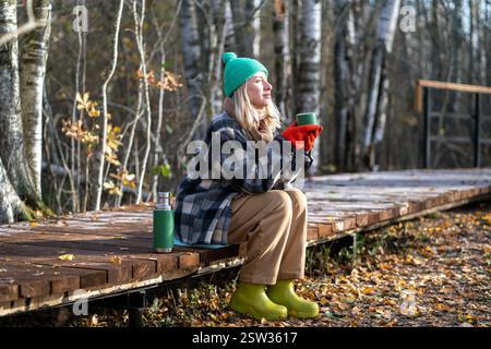 Time alone. Relaxed middle aged woman enjoy calm weekend in fall park meditative drinks thermos tea. Stock Photo