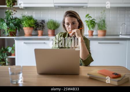 Pensive woman freelance working with laptop focused on project at home with efficiency, dedication. Stock Photo