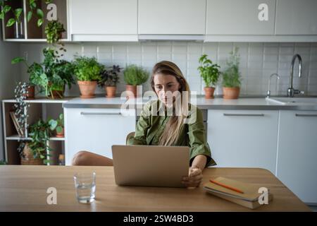 Creative focused woman freelancer online productivity working with laptop at home with houseplants. Stock Photo