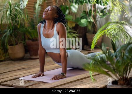 Relaxed african american woman doing snake pose, stretching body, developing flexibility on yoga mat Stock Photo