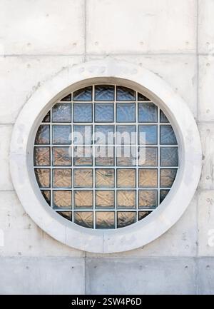 A circular glass block window embedded in a modern concrete wall. The window features a grid of textured glass bricks, allowing natural light to pass Stock Photo