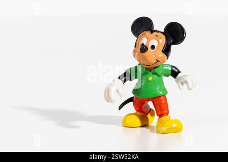 Small vintage Mickey Mouse figurine wearing green shirt and red pants standing on a white background Stock Photo