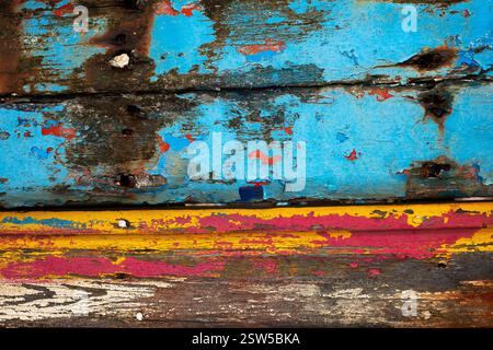 Flaking away: layers of bright blue, red and yellow paint slowly vanish from the rotting hull of a long-abandoned wooden fishing boat beached on Le Sillon (The Furrow), a causeway leading to the former sardine and scallop fishing port of Le Fret on the northern shores of the Crozon peninsula in Finistère, Brittany, France. Stock Photo