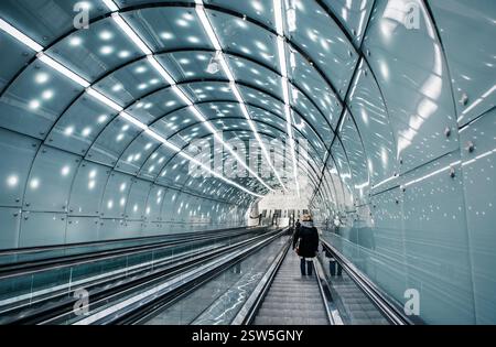 Moving escalator in subway station. Futuristic blue glass tunnel with three moving staircases and lots of lights in underground station. Stock Photo