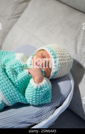 Newborn baby sleeping peacefully in a bassinet, wearing a knitted turquoise and white sweater and hat Stock Photo