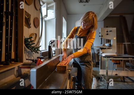 Concentrated female carpenter work with planer, trimming wood for furniture project in workshop Stock Photo