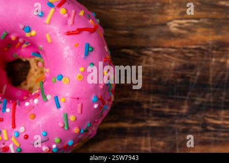 Pink donut with sprinkles on wooden background. Top view Stock Photo