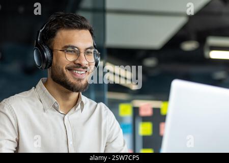 A young professional is smiling while participating in a video call in a modern office setting, showcasing remote work Stock Photo