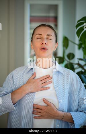 Focused on breathing middle aged woman holding hands on chest and belly doing pranayama techniques. Stock Photo