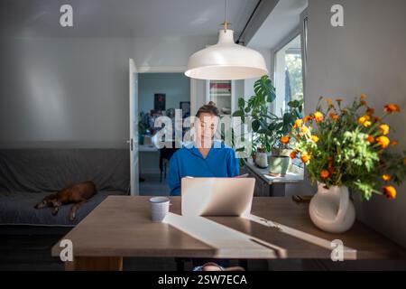 Thoughtful woman of middle age working at laptop from home office. Remote working. Stock Photo