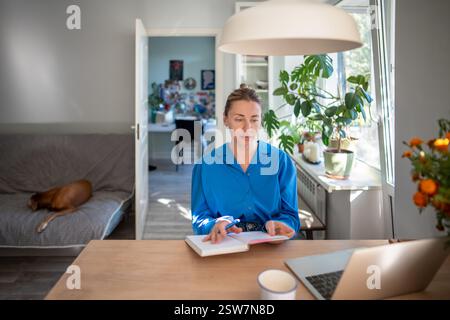 Home office middle aged woman using laptop for online meeting at cozy workplace holding day planner Stock Photo