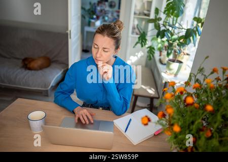 Thoughtful woman using laptop at home for remotely work, online education, comfort daily activities. Stock Photo