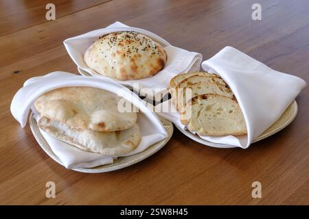 Assortment of freshly baked bread including round loaves and flatbreads served on plates with white napkins Stock Photo