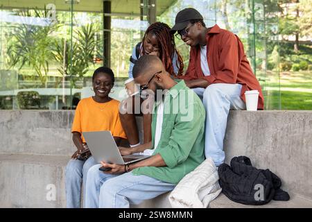 Company of satisfied happy African American students studying outside using laptop computer. Stock Photo