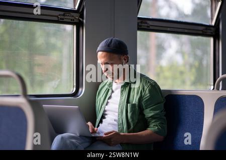 Focused man freelancer remote works on laptop riding in electric train using internet in train car. Stock Photo