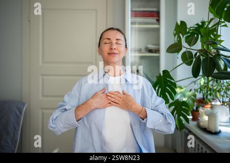 Relaxed smiling woman meditates with hands on chest, practice breathing exercises at home. Self care Stock Photo
