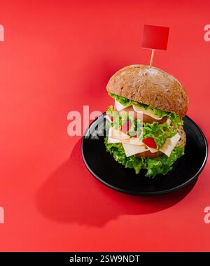 Delicious double burger standing on black plate with sausage on red background Stock Photo