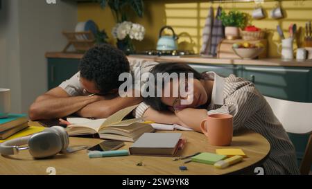 African American guy girl sleeping on kitchen table together studying at home woman man teens high school students boring study tired exhausted sleep Stock Photo