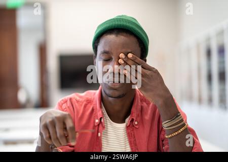Tired stressed African guy student sitting in library massaging eyes feeling unmotivated to study Stock Photo