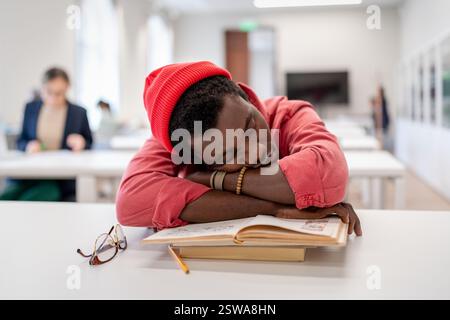 Lazy African male student falling asleep during study in library, sitting at desk sleeping on books Stock Photo