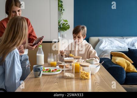 Mother and daughter using mobile phone while having breakfast together with family Stock Photo