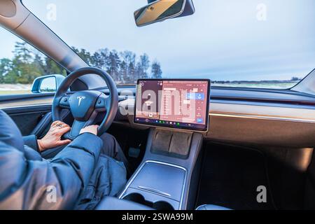 Close-up view of driver holding steering wheel inside Tesla Model 3 electric car with touchscreen displaying vehicle controls. Sweden. Stock Photo