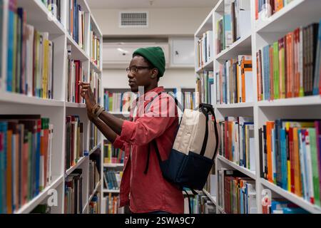 Thoughtful African American student man in glasses choosing book in college library or bookstore Stock Photo
