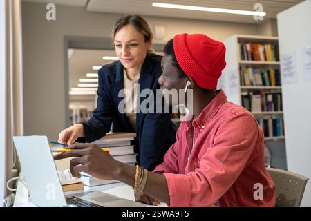 Couple multiethnic pleased students working as team on research project in library for scholarship. Stock Photo