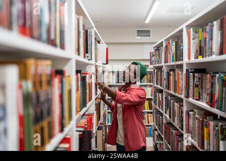 Thoughtful African American student man in glasses choosing book in college library or bookstore Stock Photo