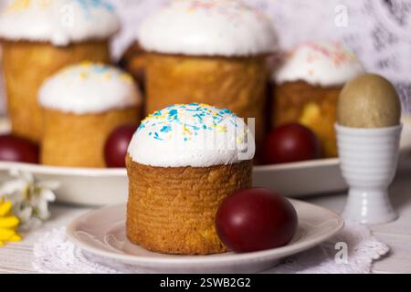 Easter bread with icing and yellow-blue sprinkles on a table with Easter eggs and spring flowers. Food for Easter Stock Photo