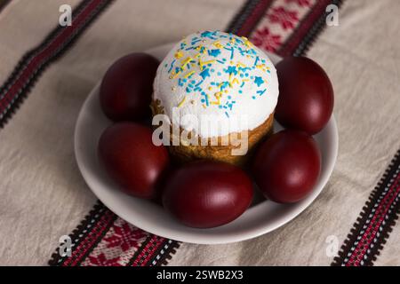 Traditional Easter bread sprinkled with yellow and blue sprinkles and krasanky (painted eggs) on a background with Ukrainian ornaments Stock Photo