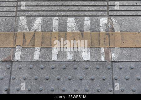 A pedestrian crossing, marked "MIND" in faded white paint, on a gray concrete sidewalk.  Likely in a European city. Stock Photo