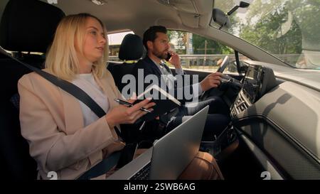Business couple Caucasian man woman workers businessman businesswoman female male auto driving to work hurry lateness using laptop in car automobile Stock Photo