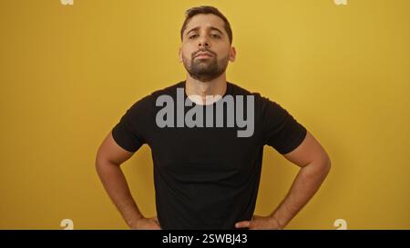 Confident young hispanic man standing isolated against a vibrant yellow background showcasing a modern and stylish look in a casual black shirt. Stock Photo