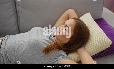 Woman relaxing on a comfortable sofa in a cozy living room, smiling peacefully, enjoying a quiet moment at home, showcasing modern interior design and Stock Photo