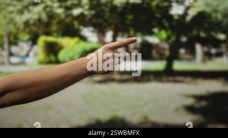 Man pointing hand outdoors on a city street, highlighting a focused gesture against a blurred urban background, suggesting direction or indication in Stock Photo