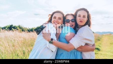 Portrait of three cheerful smiling women embracing during outdoor walking. They looking at the camera. Woman friendship, relations, and happiness conc Stock Photo