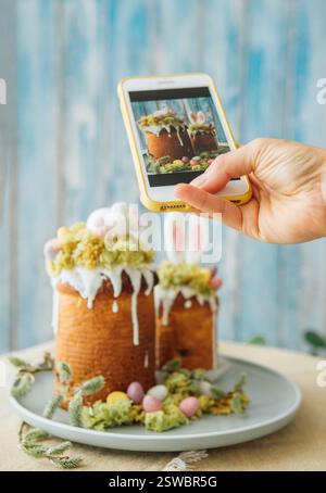 Food bloger making photo using modern smartphone. Paska - the Easter Eve sweet bread with icing decorated with eatable "moss" still life. Popular dess Stock Photo