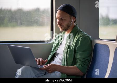Focused tech savvy businessman type on laptop, wearing earphones while traveling by train to work Stock Photo