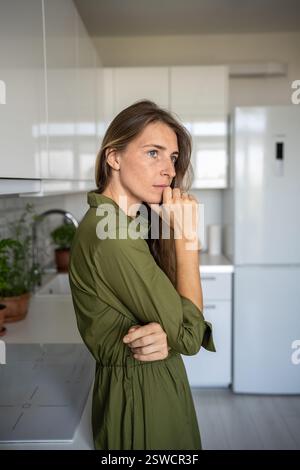 Depressed frustrated middle aged woman thinking about difficult problems standing at home in tension Stock Photo