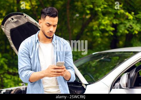 Sad arab man looking for auto service, using smartphone Stock Photo