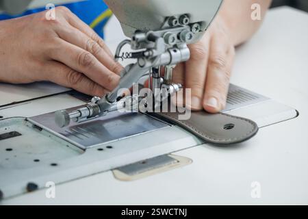 Hands guiding leather under sewing machine needle crafting with precision on a clean white surface Stock Photo