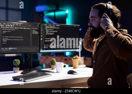 Programmer enjoying podcasts and futureproofing company network from downtimes and unexpected system failures. IT expert putting headphones on to listen audiobooks while increasing data security Stock Photo