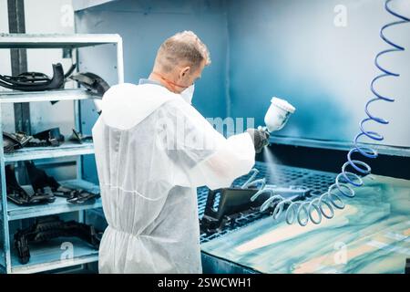 Protective gear worker using spray gun in a painting booth Automotive part manufacturing process Stock Photo