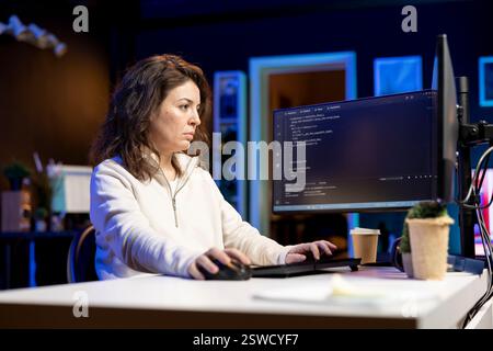Woman in living room working from home implementing security measures to protect company systems and data. Tech support staff member writing, testing and debugging code for software applications Stock Photo