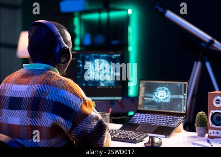 Professional male developer manages neural network at desk, working with AI code on laptop. African american IT expert freelancer developing cyber security, creating secure database. Stock Photo