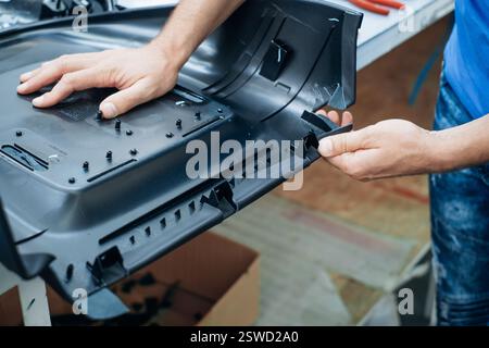 A person works with their hands assembling an intricate black plastic component in an industrial setting Stock Photo