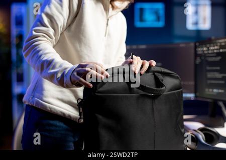 Developer closing laptop, ready to go home after designing and developing software applications. IT professional packing notebook in bag after implementing and maintaining company systems Stock Photo