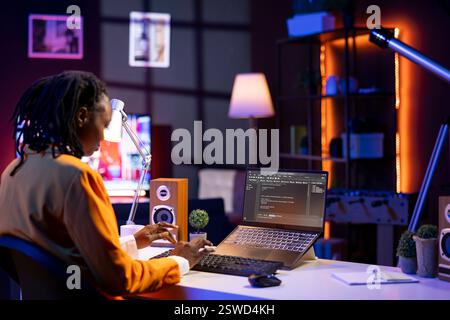 Software developer writes code on laptop screen while in apartment office using Java programming languages. Programmer remotely working on fixing database errors while working from home Stock Photo