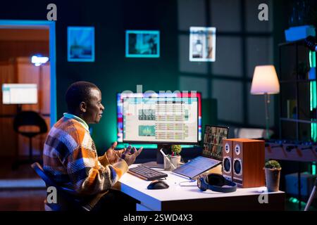 Black man waving on video call and discussing about business infographics, reviewing monthly budget balance and working remotely. Staff focused on conversation during online meeting on pc. Stock Photo